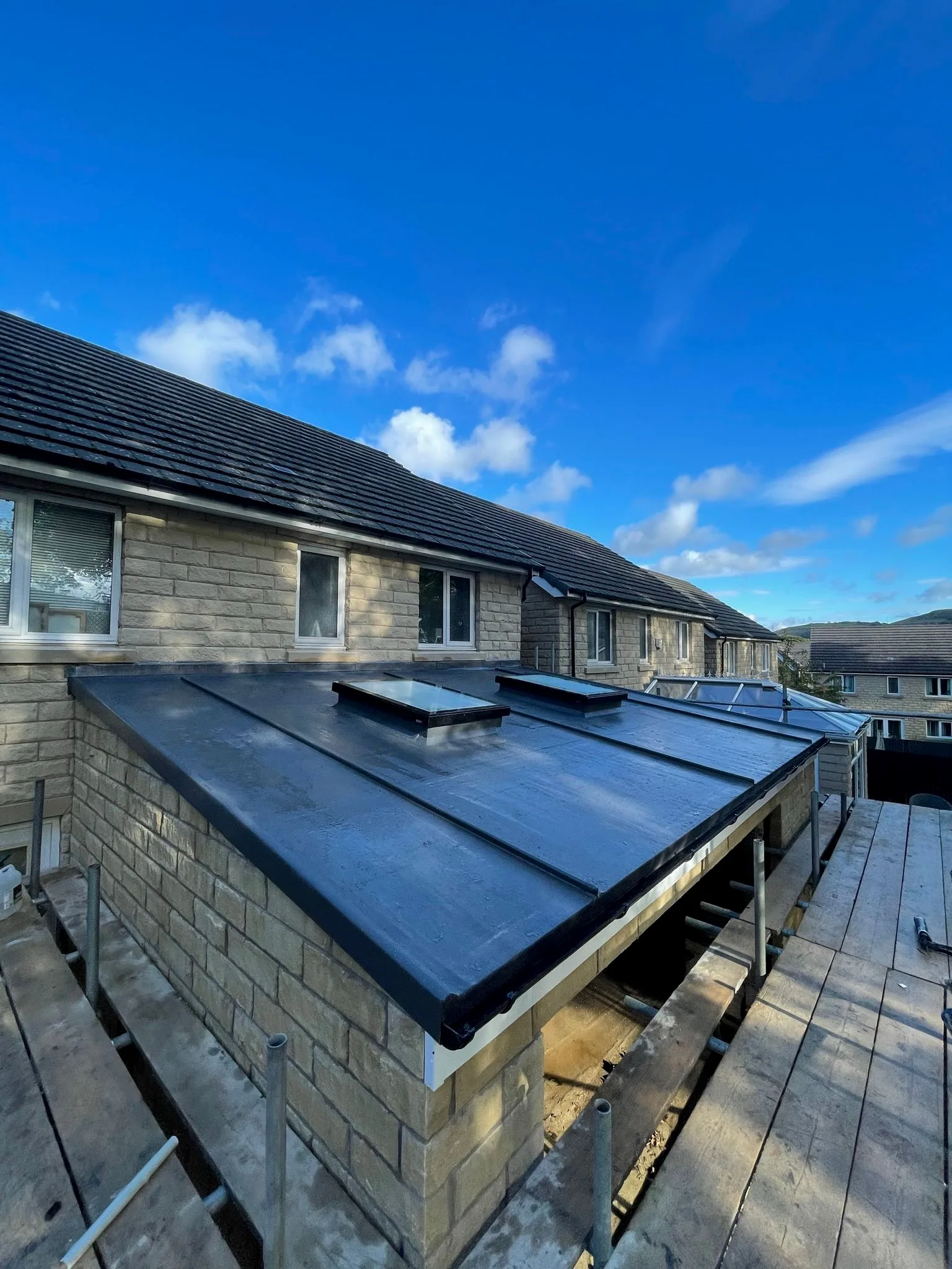 Blue membrane roof with two skylights on stone house under clear sky